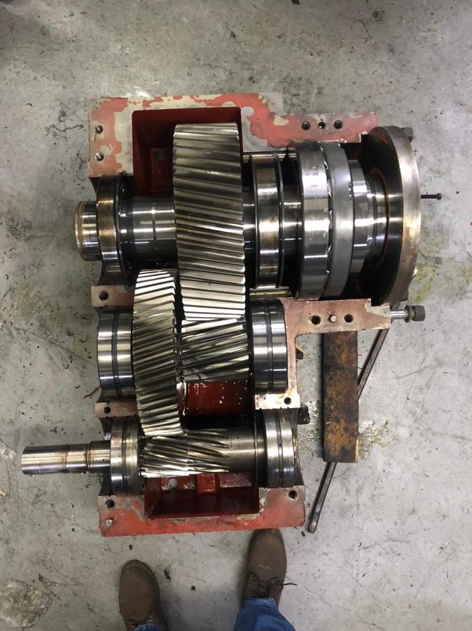 Industrial gearbox opened up showing helical gears and bearings during teardown
