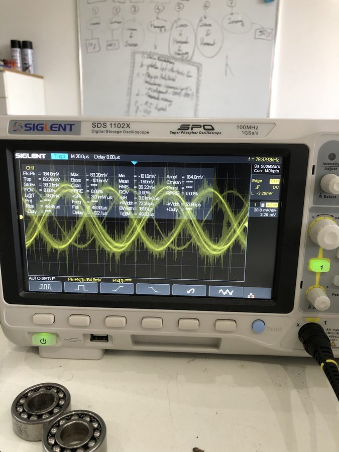Siglent oscilloscope showing an accelerometer vibration waveform, with ball bearings on the bench